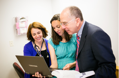 two women and a man look at a computer