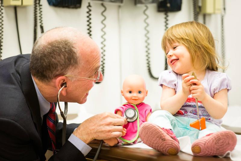 a pediatrician holding a stethoscope smiling at a smiling young girl